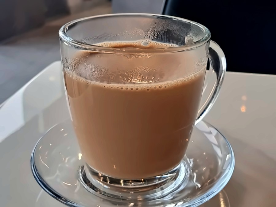 A glass mug of classic karak on a saucer at Karak Junction
